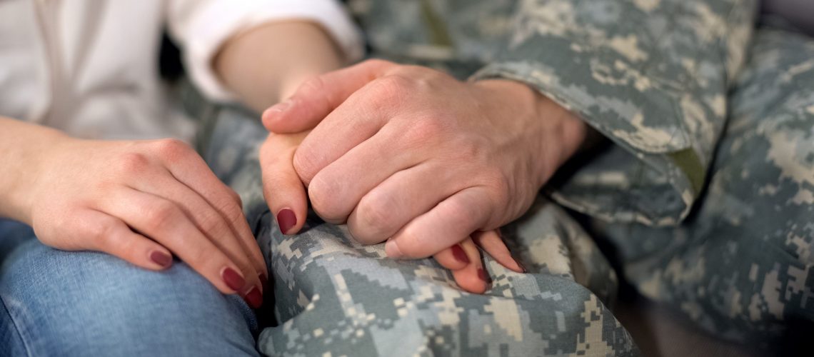 Military spouse holding husband's hand.