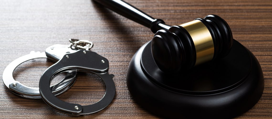 Gavel and handcuffs on wooden table.