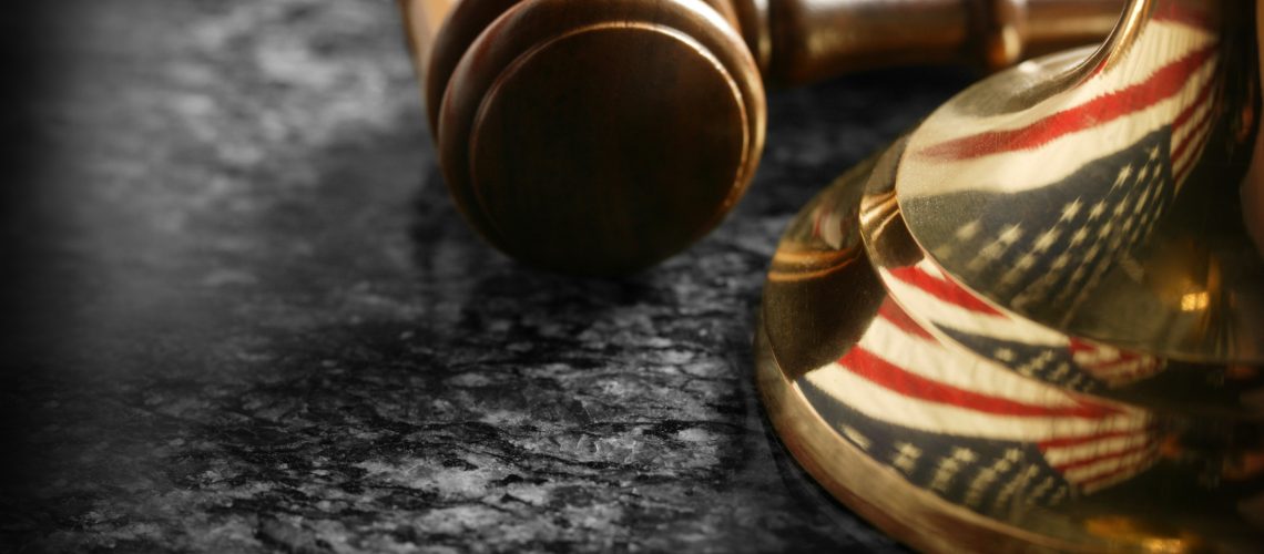 A gavel and the American flag reflected in the base of a justice scale