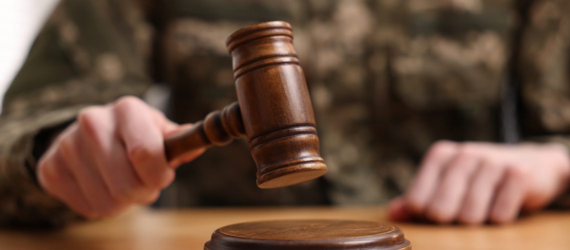 Law concept. Man in military uniform with gavel at wooden table, closeup