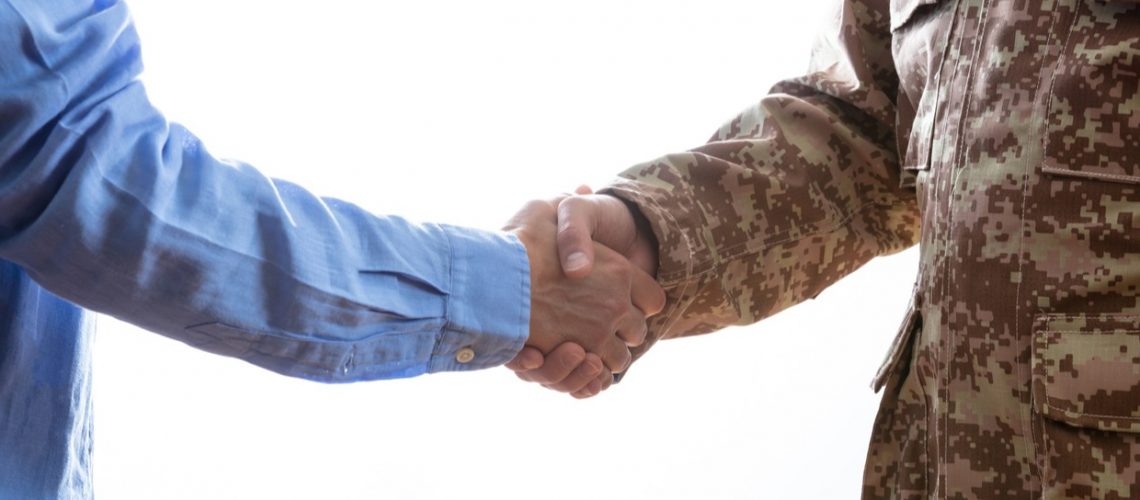 Military person and civilian shaking hands standing on white background