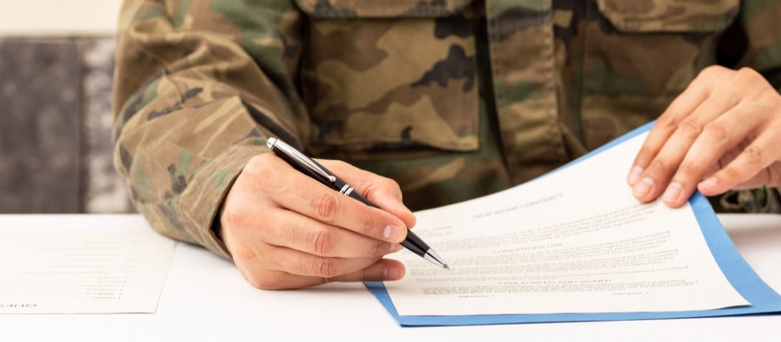 Close up of executive military man hands signing contract on a desk at work