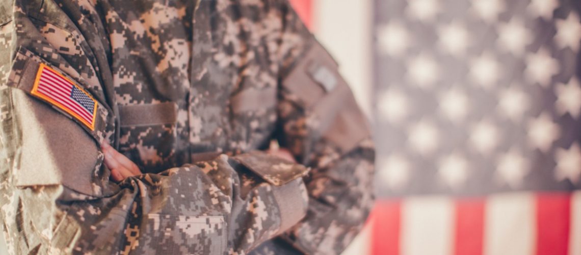 national guard member standing in front of an American flag with arms crossed